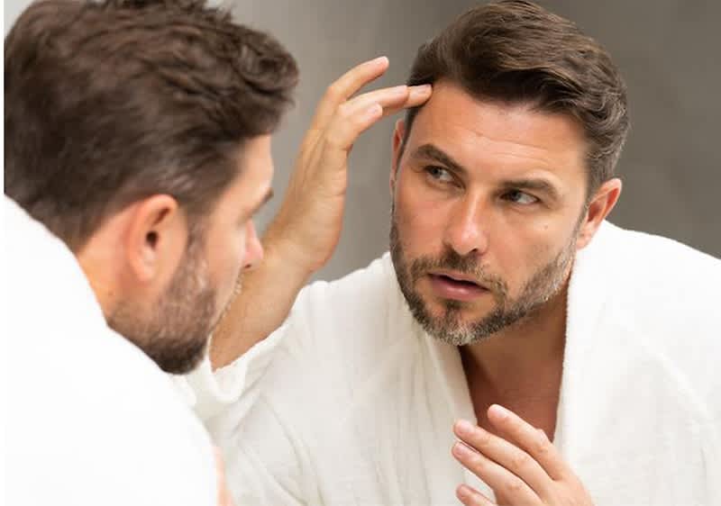 Mann im Bademantel betrachtet sich im Spiegel