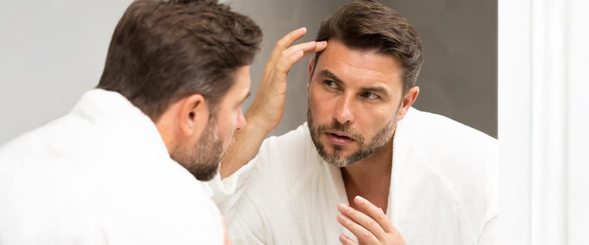 Mann im Bademantel betrachtet sich im Spiegel