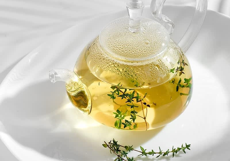 Kräutertee in Glasteekanne mit frischem Thymian auf weißem Teller
