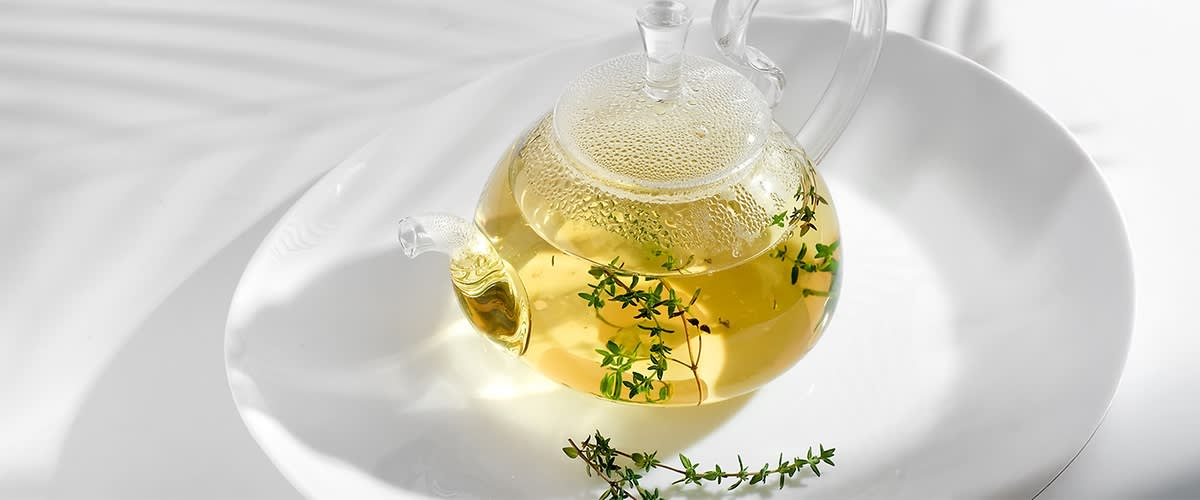 Kräutertee in Glasteekanne mit frischem Thymian auf weißem Hintergrund