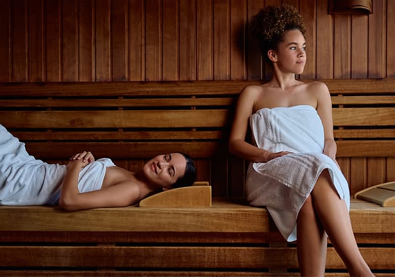 Sauna mit zwei Personen in weißen Handtüchern auf Holzbänken