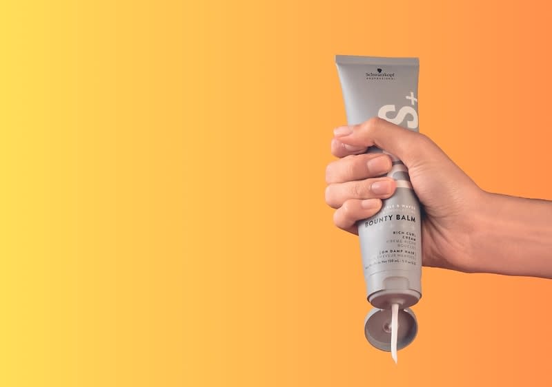 Hand hält eine Tube Haarpflegecreme vor orangefarbenem Hintergrund