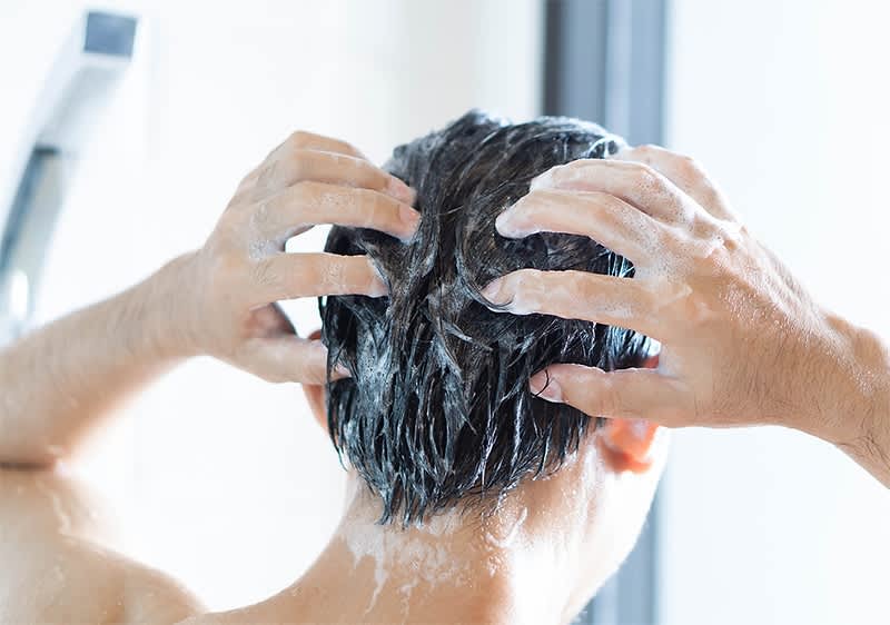 Mann wäscht Haare mit Shampoo im Badezimmer