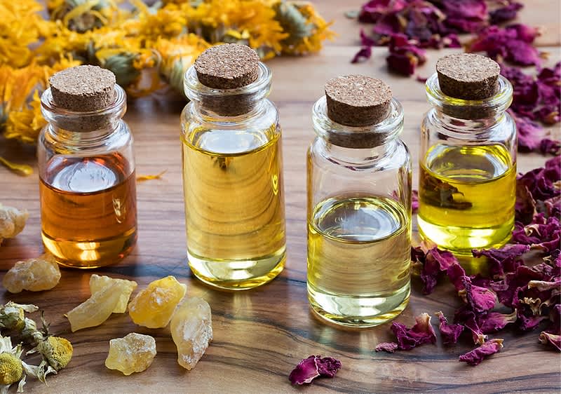 Ätherische Öle in Glasflaschen mit getrockneten Blumen und Harz auf Holztisch