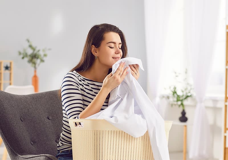 Frau riecht frisch gewaschene Wäsche in einem Korb im Wohnzimmer