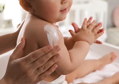 Babyhautpflege mit Creme auf Schulter und Händen