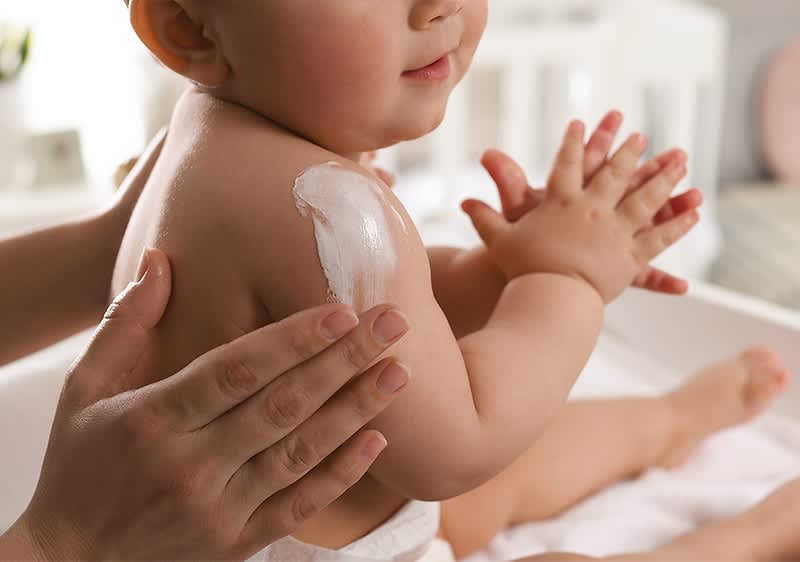 Babyhautpflege mit Creme auf Schulter und Händen
