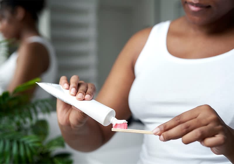 Zahnpasta auf Zahnbürste von Frau in weißem Top
