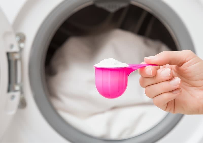 Waschmittel vor Waschmaschine mit Wäsche im Hintergrund