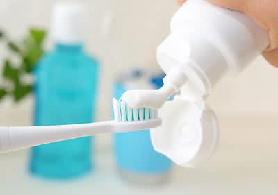 Zahnpasta auf Zahnbürste mit Mundwasser im Hintergrund