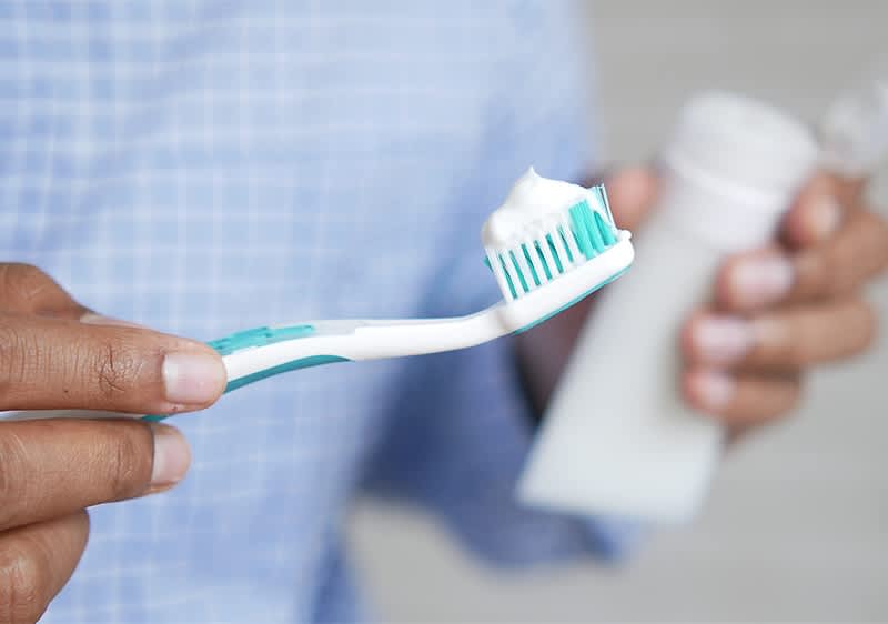 Zahnpasta auf Zahnbürste in Hand mit Zahnpastatube im Hintergrund