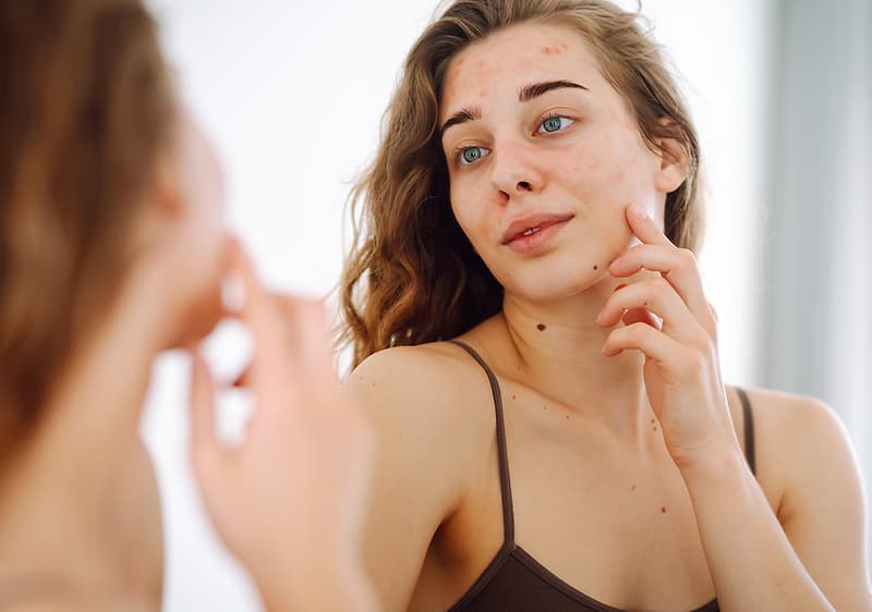 Frau betrachtet sich im Spiegel mit lockigem Haar und braunem Top