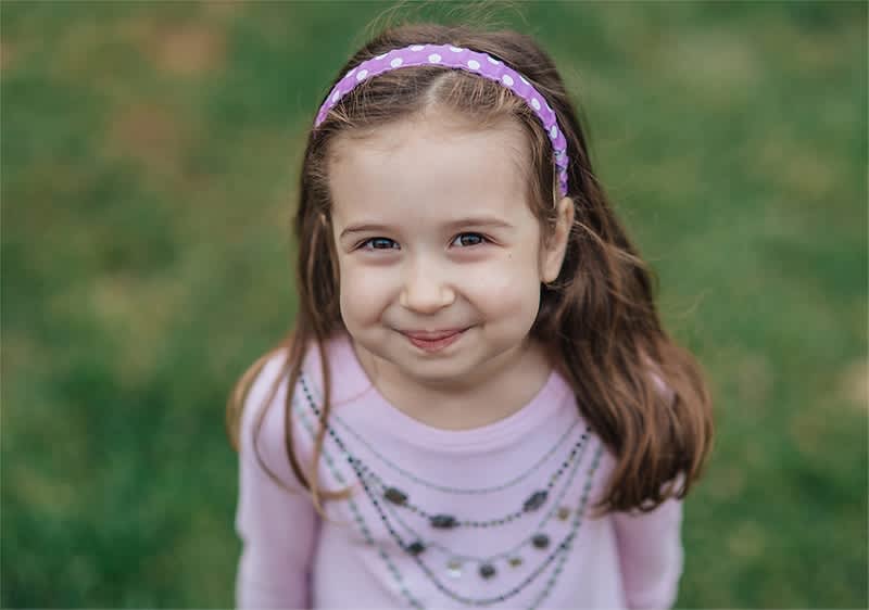 Kind mit lila Haarband und rosa Oberteil auf grünem Hintergrund