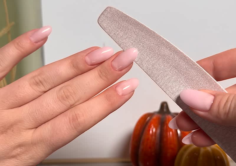 Nagelpflege mit Feile und Kürbis-Dekoration im Hintergrund