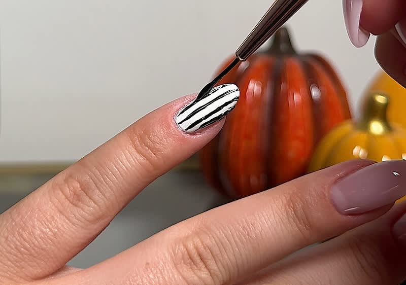 Nageldesign mit schwarz-weißen Streifen vor Kürbisdekoration