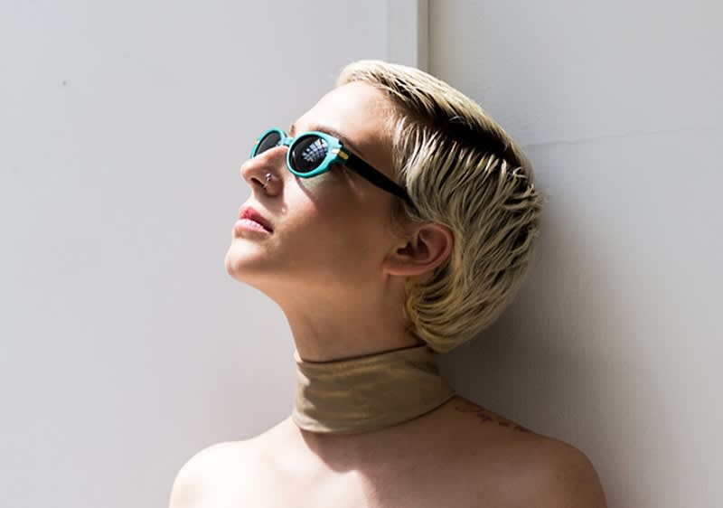 Frau mit kurzen blonden Haaren Sonnenbrille steht an einer Wand