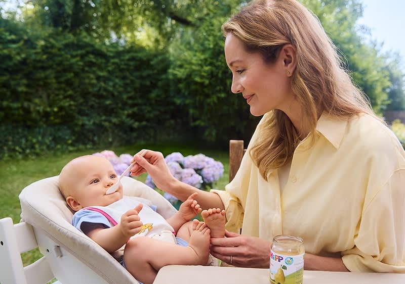 Frau füttert Baby im Garten mit Babynahrung