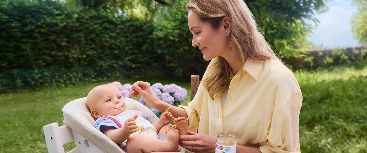 Frau füttert Baby im Garten mit Babynahrung