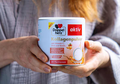 Eine Dose Doppelherz aktiv Kollagenpulver mit Vitamin C, Zink und Biotin, Aufschrift „20 Portionen“, wird von einer Person gehalten