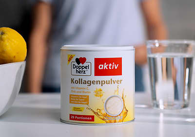 Eine Dose Doppelherz aktiv Kollagenpulver mit Vitamin C, Zink und Biotin, daneben ein Glas Wasser und eine Zitrone in einer Schale