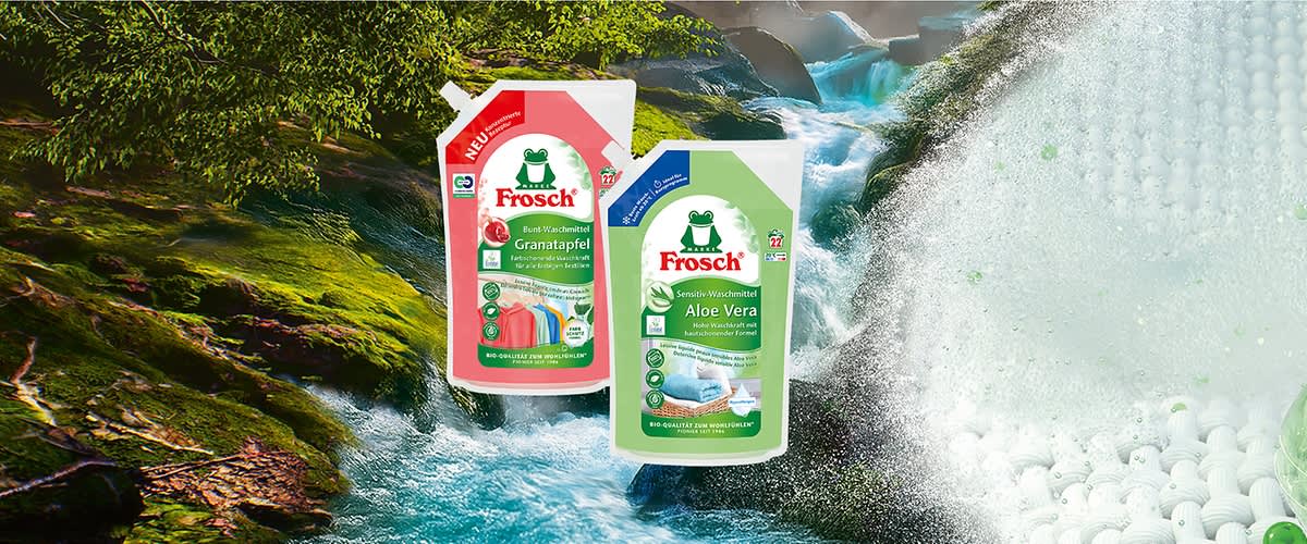 Zwei Frosch-Nachfüllbeutel für Waschmittel, links rot mit Aufschrift „Granatapfel“ und rechts grün mit Aufschrift „Aloe Vera“, darüber das Frosch-Logo, im Vordergrund grüne Kappe und Symbole für 100% recyceltes Material und Ökolabel, im Hintergrund Wasserfall und Fluss. Bild mit AI erstellt