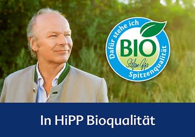 Herr Hipp in traditioneller Kleidung steht vor einem grünen Hintergrund. Rechts daneben das HiPP Bio-Logo mit dem Text „Dafür stehe ich, Spitzenqualität“. Darunter der Schriftzug „In HiPP Bioqualität“ auf blauem Hintergrund