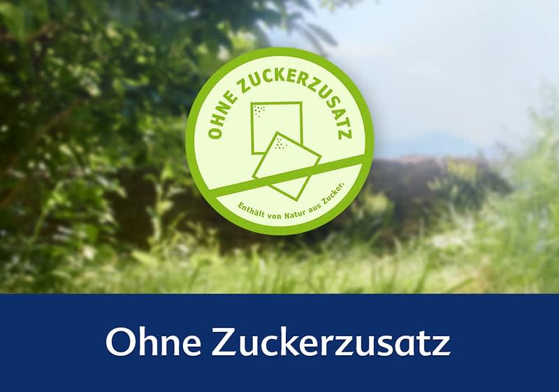 Ein grünes Siegel mit der Aufschrift „Ohne Zuckerzusatz“ und „Enthält von Natur aus Zucker“ auf einem unscharfen Naturhintergrund