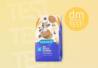 Eine Packung babylove Bio Haffeln Blaubeere mit einem Waschbär, blauen Beeren und der Aufschrift „dm Produkttest“ auf gelbem Hintergrund