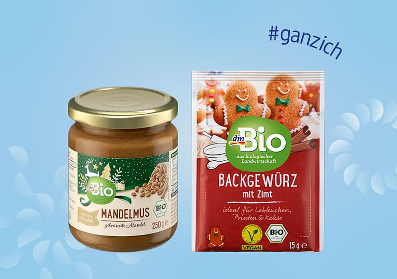 Links ein Glas dmBio Mandelmus mit braunem Etikett, rechts eine Packung dmBio Backgewürz mit Zimt, oben der Hashtag #ganzich