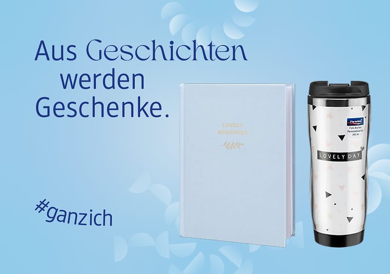 Ein hellblaues Buch mit der Aufschrift „Lovely Memories“ und ein weißer Thermobecher mit „Lovely Day“ daneben. Text: „Aus Geschichten werden Geschenke“ und „#ganzich“