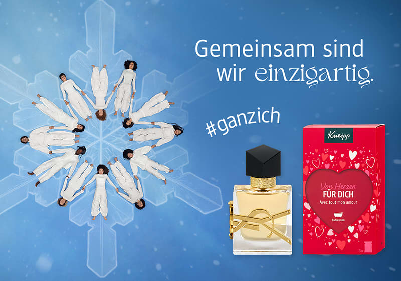 Eine Schneeflocken-Formation aus tanzenden Personen, daneben ein Parfümflakon und eine rote Verpackung mit der Aufschrift „Von Herzen FÜR DICH“ sowie „#ganzich“ und „Gemeinsam sind wir einzigartig“
