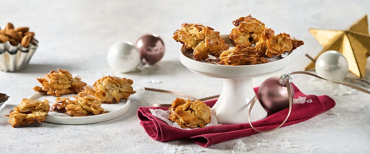 Florentiner Kekse mit Mandeln auf einer weißen Tortenplatte, daneben Weihnachtskugeln und ein rotes Tuch