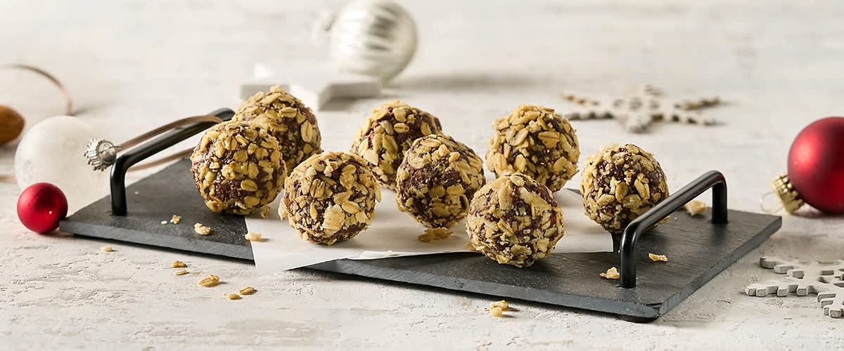 Acht Schokoladenkugeln mit Haferflocken auf einem schwarzen Tablett, im Hintergrund eine silberne Weihnachtskugel und ein weißer Stern aus Holz