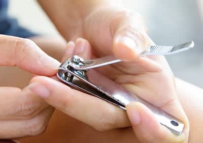 Eine Person schneidet mit einem silbernen Nagelknipser einen Fingernagel