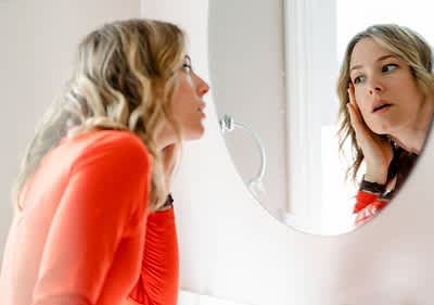 Eine Person in einem roten Oberteil betrachtet sich in einem runden Spiegel