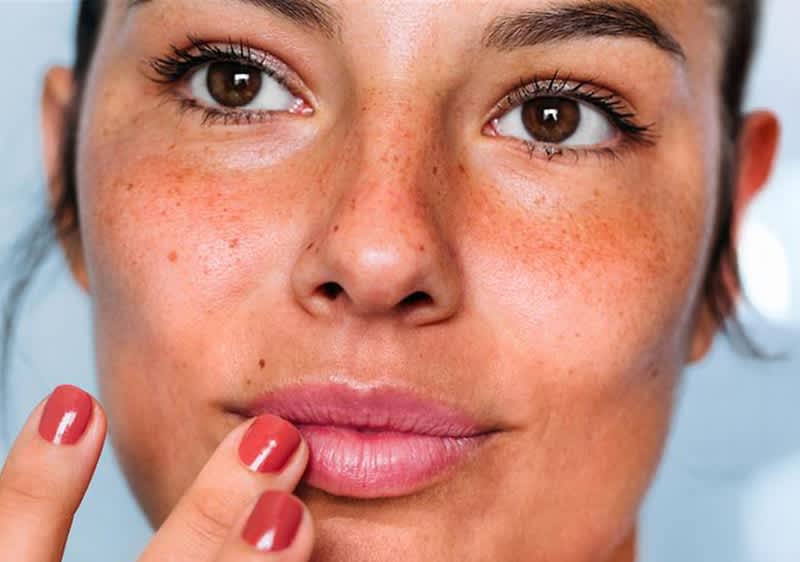 Eine Frau mit rot lackierten Nägeln berührt ihre Lippen mit einem Finger