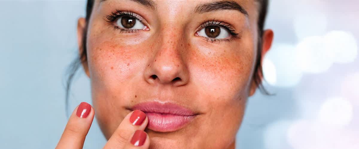 Eine Frau mit rot lackierten Nägeln berührt ihre Lippen mit einem Finger