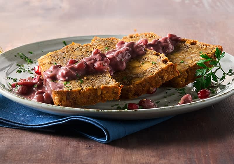 Drei Scheiben vegetarischer Braten mit roter Sauce und Petersilie auf einem weißen Teller mit blauem Stoff darunter