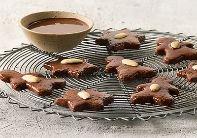 Mehrere Lebkuchen in Sternform mit Mandeln darauf liegen auf einem runden Gitter neben einer Schale mit Schokoladensauce