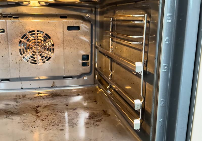 Ein geöffneter, verschmutzter Backofen mit Metallgestellen und einem Lüfter an der Rückwand