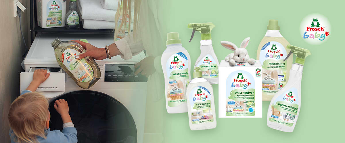 Mehrere grüne und weiße Frosch Baby Reinigungsprodukte gruppiert um eine weiße Waschpulverpackung mit einem Stoffhasen obenauf, sichtbar Waschmittel-, Vorwaschspray- und Hygienereiniger-Flaschen sowie das Frosch Baby Logo