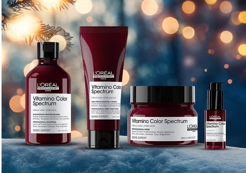 Vier L'Oréal Vitamino Color Spectrum Produkte vor einem unscharfen Hintergrund mit Lichtern, darunter Flasche, Tube, Tiegel und Pumpspender