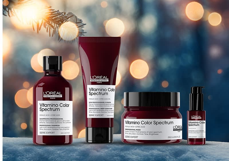 Vier L'Oréal Vitamin Color Spectrum Produkte auf Schnee, links eine Flasche, daneben eine Tube, ein Tiegel und ein Pumpspender, im Hintergrund Lichter und Zweige