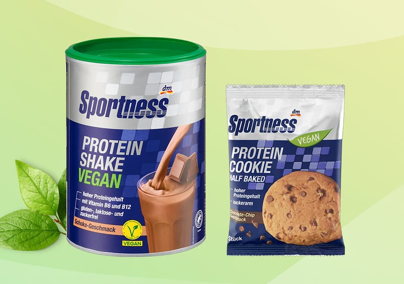 Eine grüne Dose mit der Aufschrift „Sportness Protein Shake Vegan“ und eine Packung „Sportness Protein Cookie Vegan“ vor grünem Hintergrund