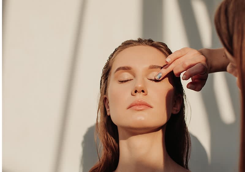 Eine Person mit langen braunen Haaren wird von einer anderen Person am Kopf berührt, Gesicht unscharf. Schatten im Hintergrund.