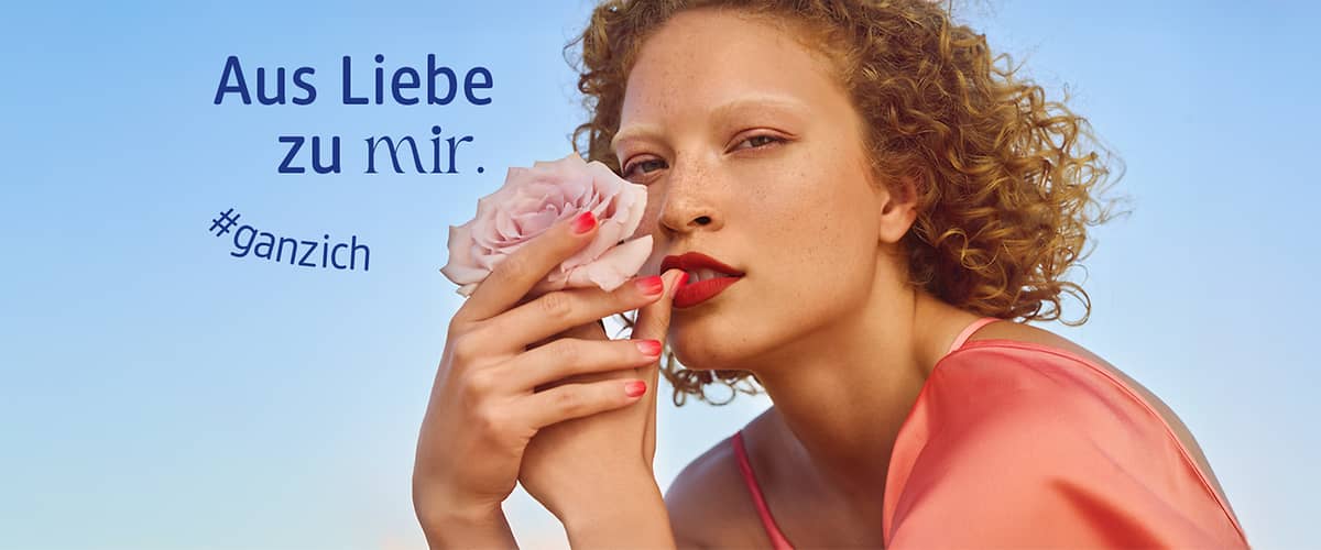 Eine Person hält eine rosa Blume. Der Text „Aus Liebe zu mir. #ganzich“ ist auf der linken Seite zu sehen.