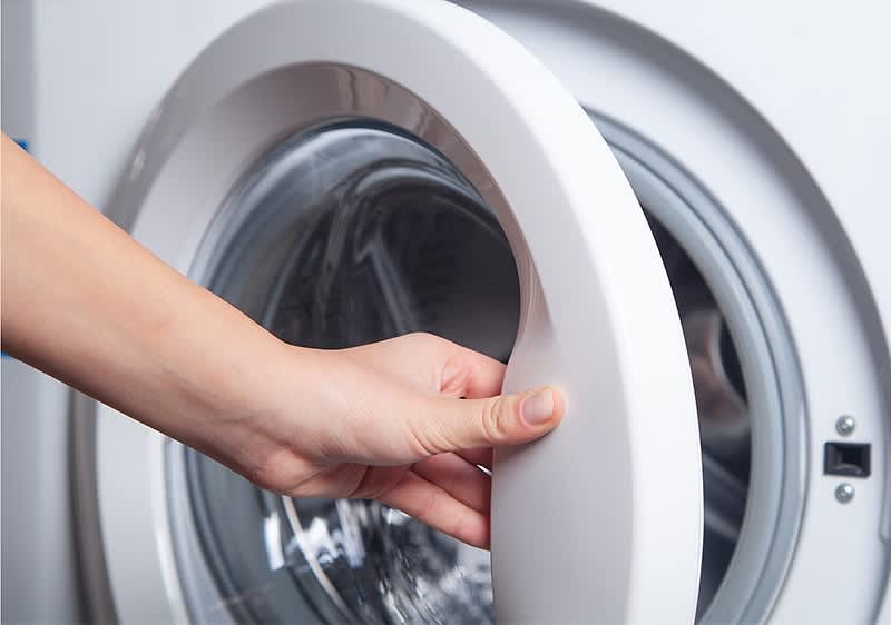 Eine Hand öffnet die Tür einer weißen Waschmaschine.