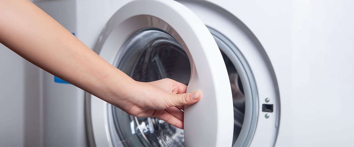 Eine Hand öffnet die Tür einer Waschmaschine.
