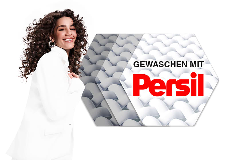 Eine Frau in weißem Blazer steht neben einem Persil-Werbeschild mit der Aufschrift „GEWASCHEN MIT Persil“ und einem Bild von weißen Stofffasern.
