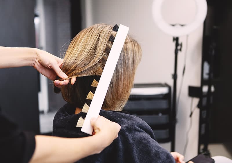 Friseurin misst mit Streifenlineal die Länge eines kinnlangen blonden Haarschnitts bei Kundin im Salon